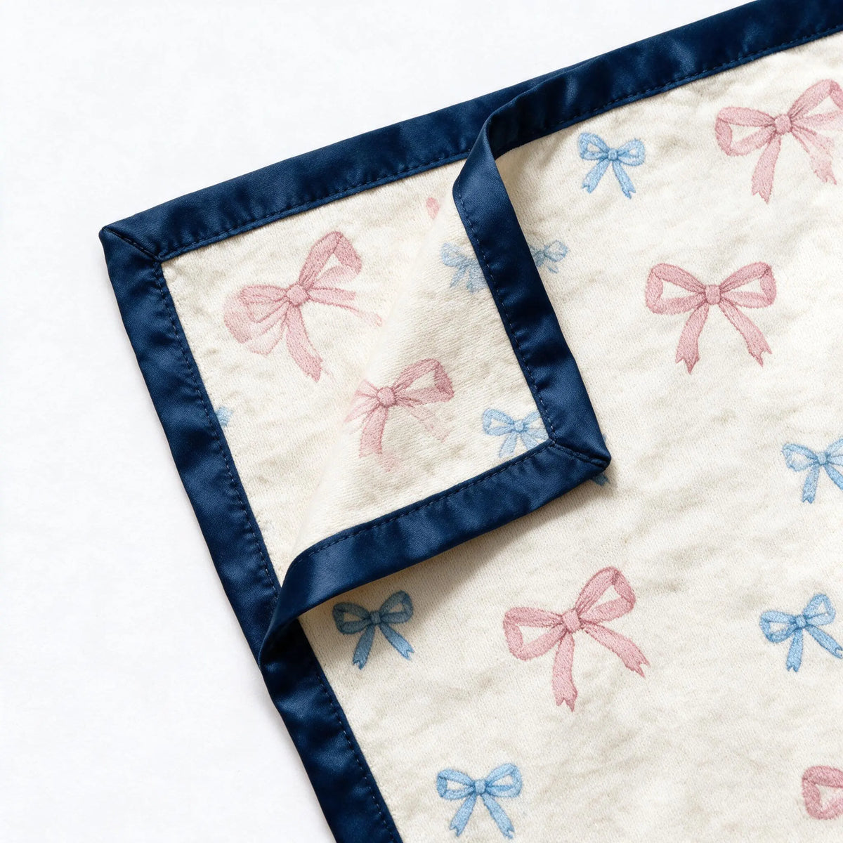 Close up photograph of the JOWI Baby Blanket on white: the corner where two edges of the navy satin binding are mitred together, with the corner turned back