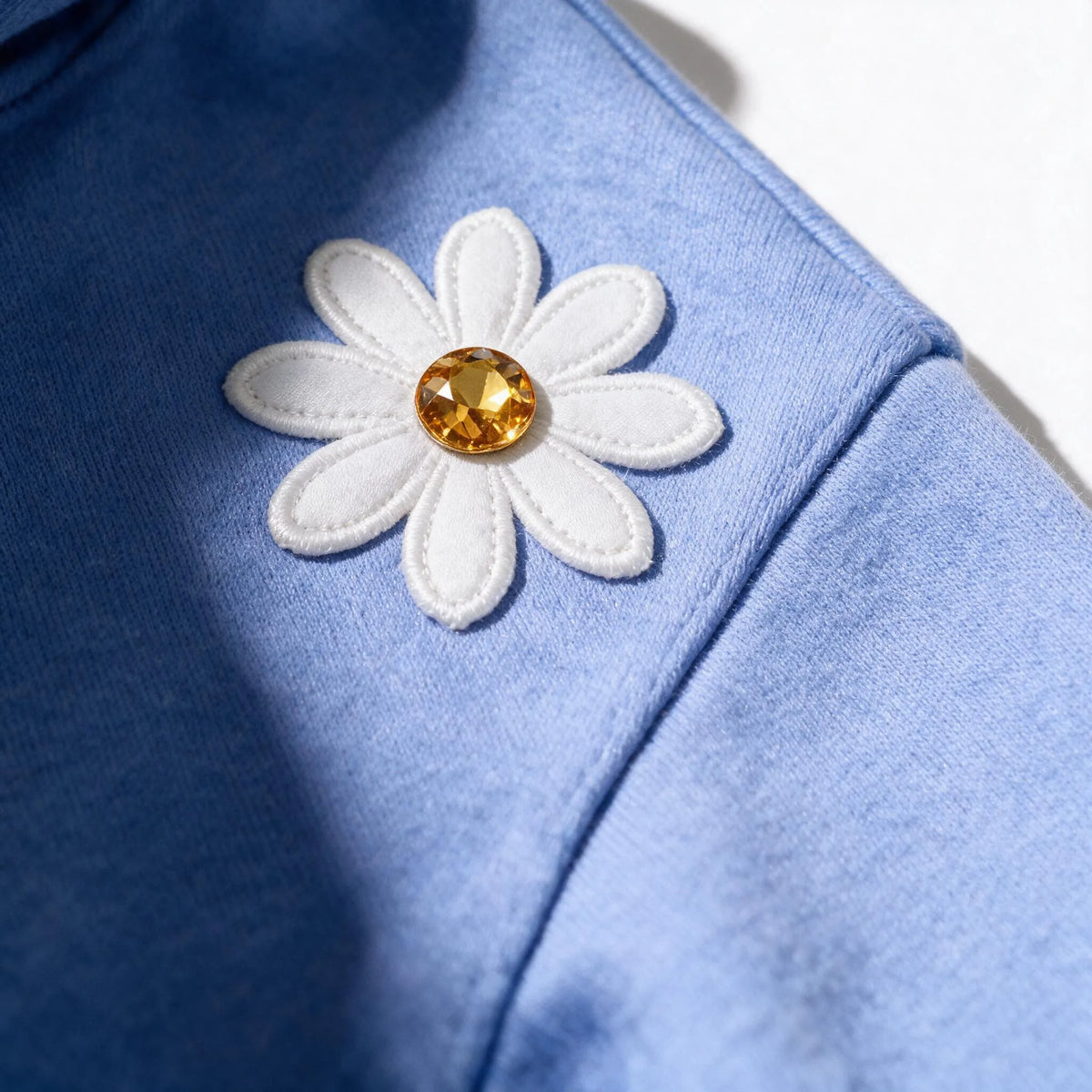 Close up photograph of the white daisy with the golden yellow centre on the chest of the JOWI Blue Daisy Hoodie & Jogger Set, with the brushed fleece at true scale