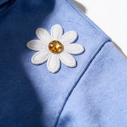 Close up photograph of the white daisy with the golden yellow centre on the chest of the JOWI Blue Daisy Hoodie & Jogger Set, with the brushed fleece at true scale