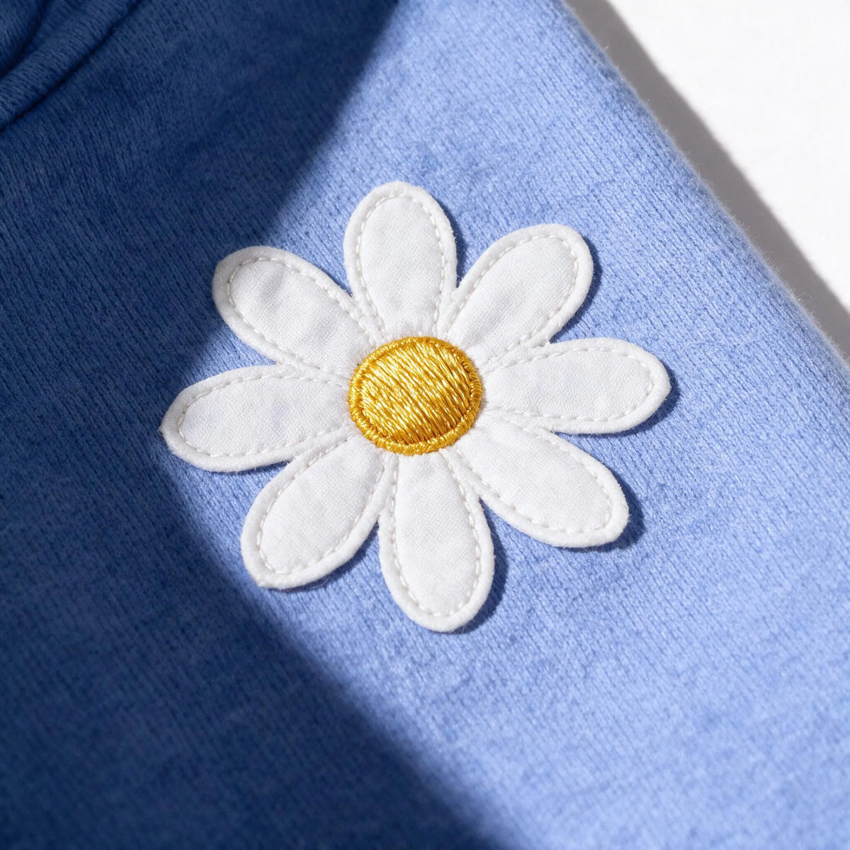 Alternative close up of the same daisy on the JOWI Blue Daisy Hoodie and Jogger Set, showing the centre worked in golden yellow thread instead of as a stone, for comparison