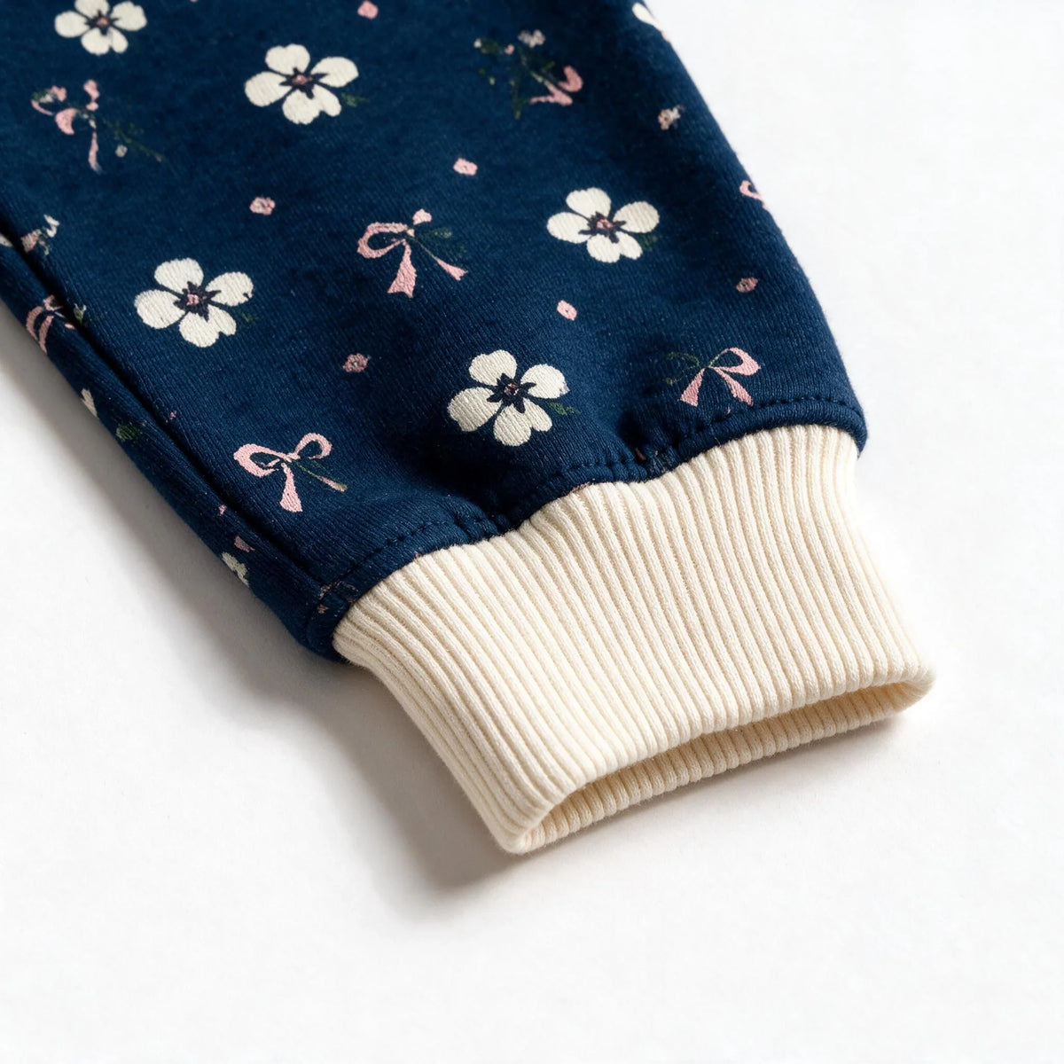 Close up photograph of the JOWI Blue Ditsy Pajama Set on white: the plain cream ribbed cuff, gathered where the navy ditsy print is eased into it