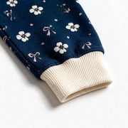Close up photograph of the JOWI Blue Ditsy Pajama Set on white: the plain cream ribbed cuff, gathered where the navy ditsy print is eased into it