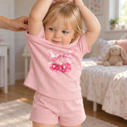 A girl pulling the tee of the JOWI Cherry Bow Tee & Short Set on over her head, showing that it has no fastening