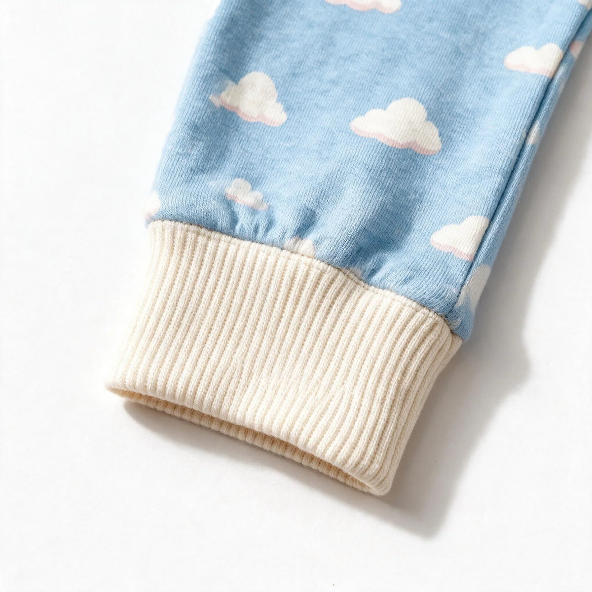 Close up photograph of the JOWI Cozy Cloud Sleepsuit on white: the plain cream ribbed cuff that closes the cloud print, with no foot beyond it