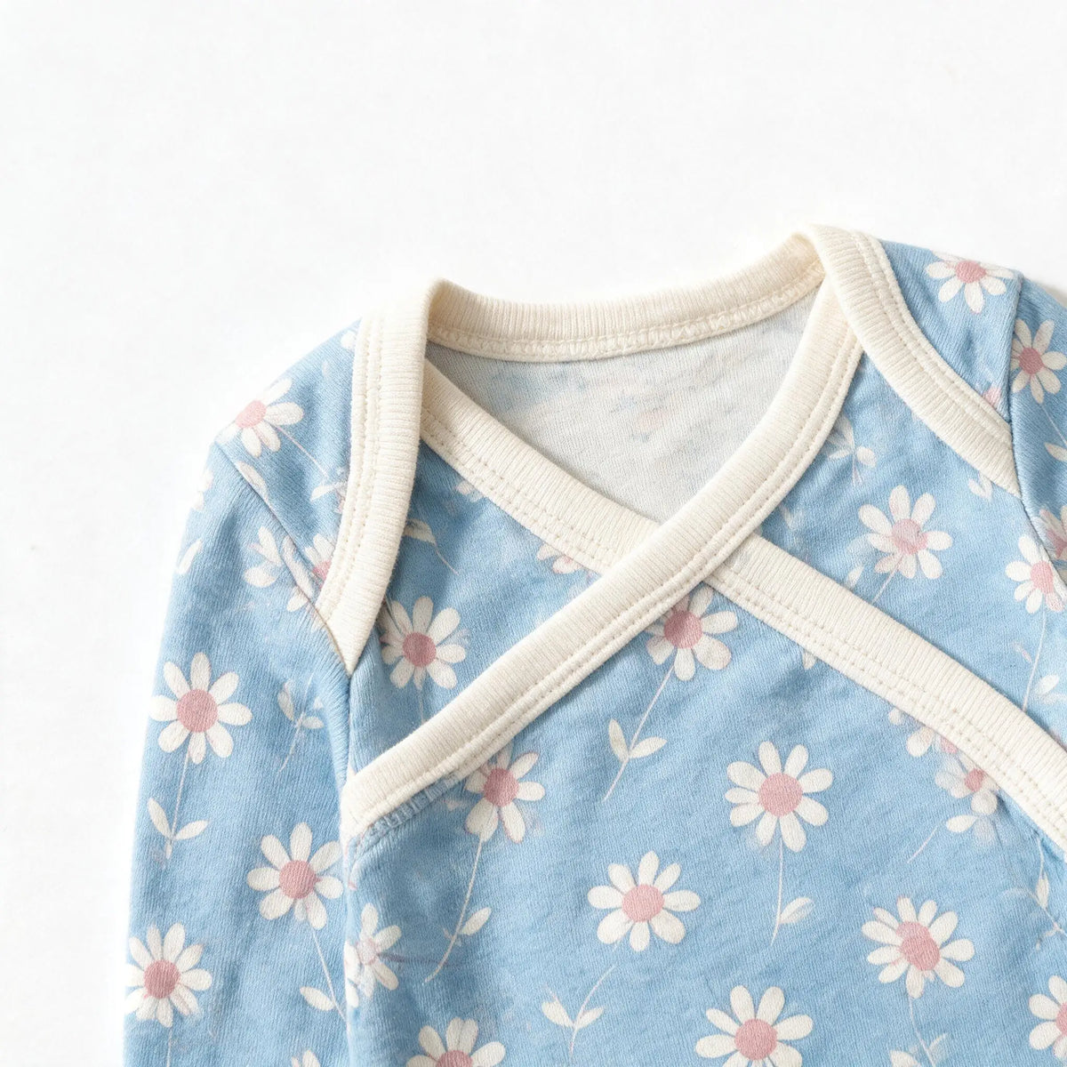 Close up photograph of the JOWI Little Daisy Bodysuit on white: the envelope neckline, with the two shoulder panels crossing over each other under their plain cream bands