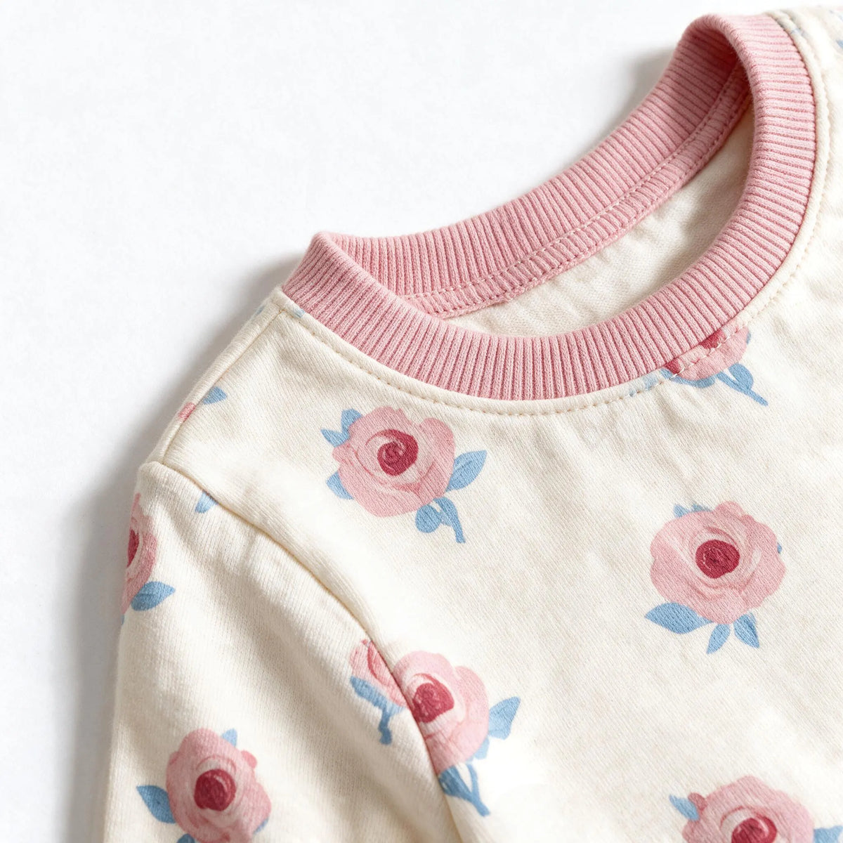 Close up photograph of the JOWI Little Rose Dress Set on white: the plain dusty pink neckband of the dress where it is stitched to the printed cloth