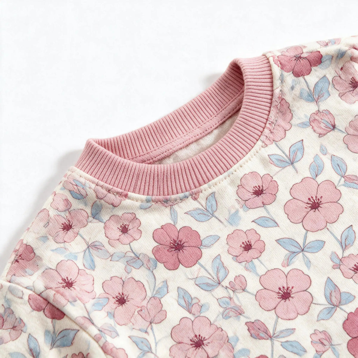 Close up photograph of the JOWI Pink Floral Pajama Set on white: the plain dusty pink ribbed crew neckband of the top
