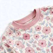 Close up photograph of the JOWI Pink Floral Pajama Set on white: the plain dusty pink ribbed crew neckband of the top