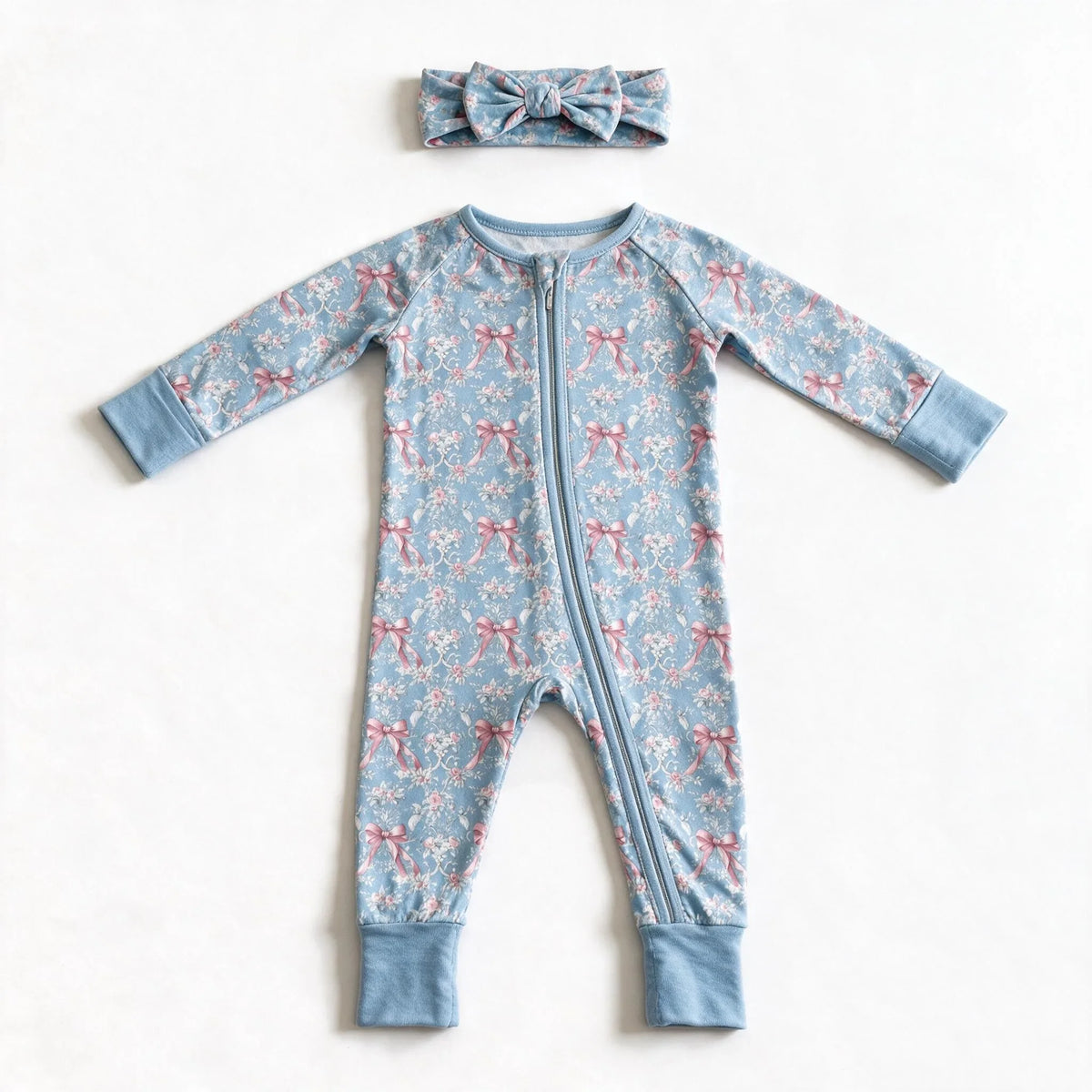Blue rose toile zip romper photographed flat on white with the matching bow headband above it, showing the two way zipper and the plain blue cuffs