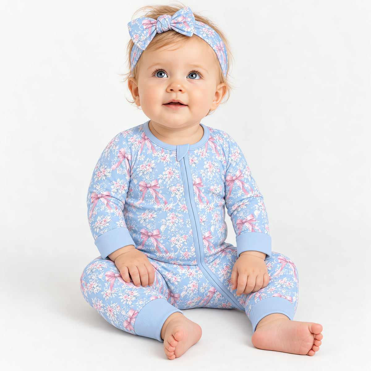 Baby sitting up wearing the blue rose toile zip romper and the matching bow headband