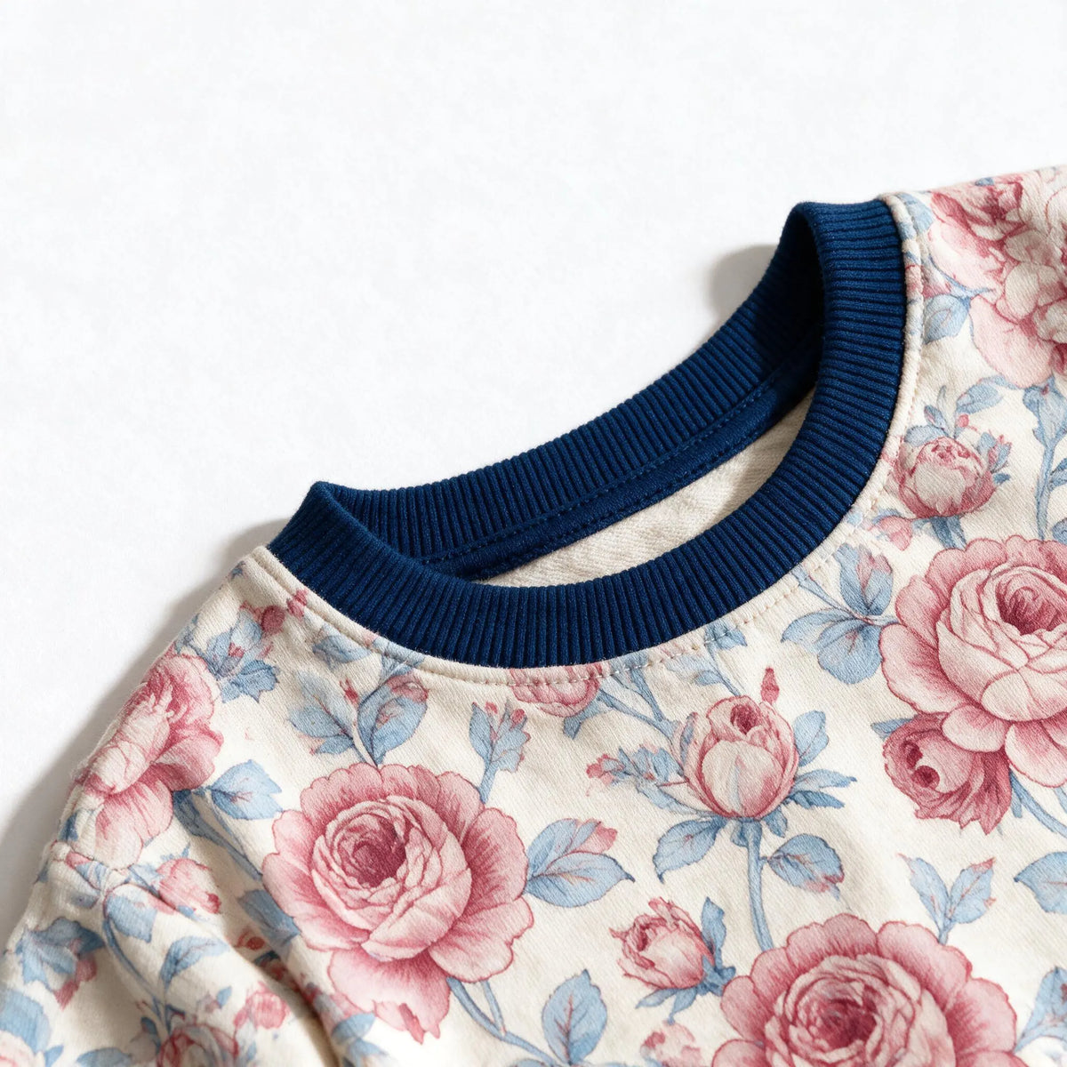 Close up photograph of the JOWI Rose Garden Pajama Set on white: the plain navy ribbed crew neckband of the top