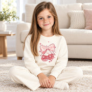 Girl sitting cross legged in the cream cherry bow sweatshirt and jogger set