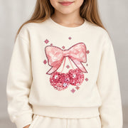 Close up of the pink sequin bow and cherries on the cream sweatshirt, sleeves plain