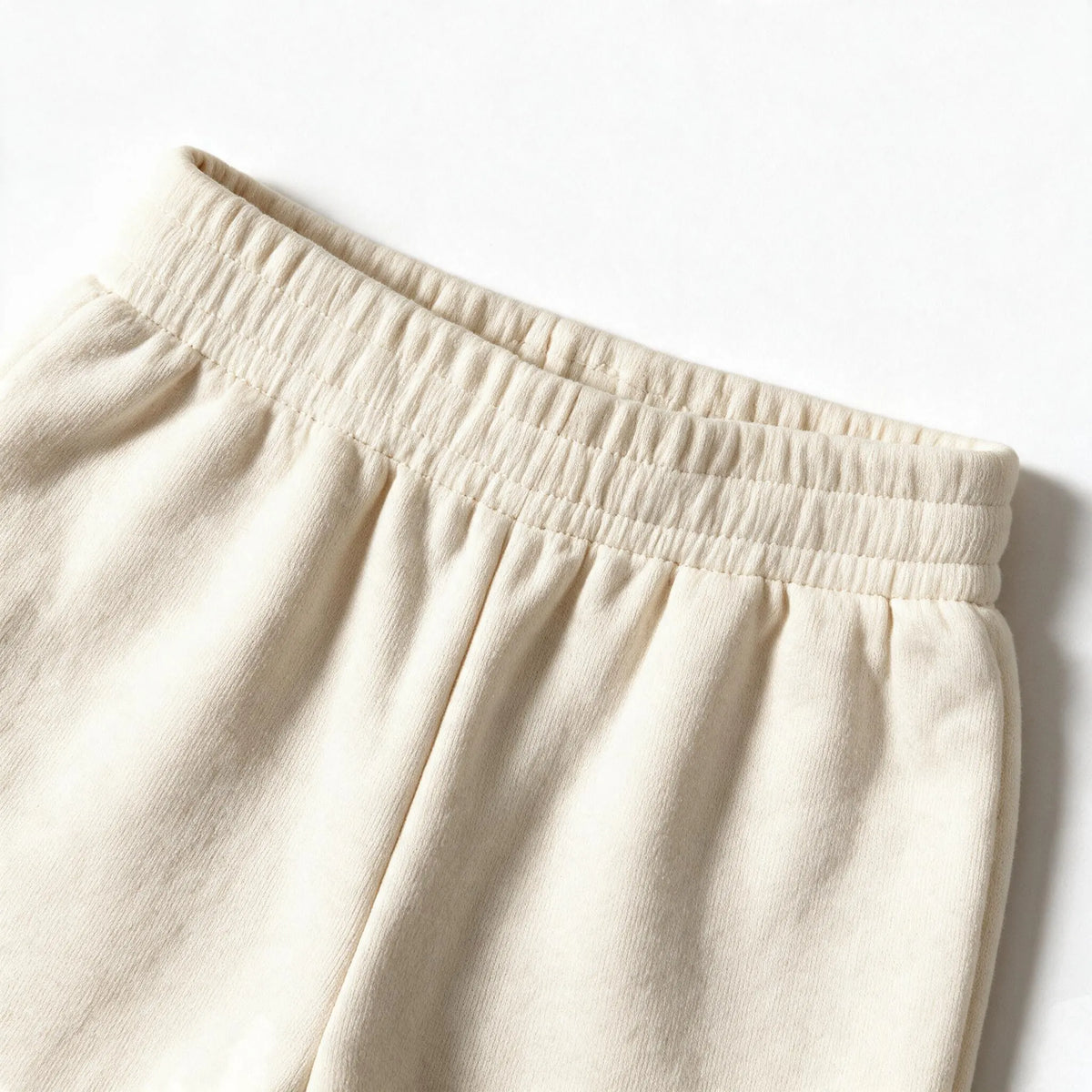 Close up photograph of the JOWI Cherry Bow Sweatshirt & Jogger Set on white: the flat elastic waistband of the cream joggers, with the terry gathered softly below it