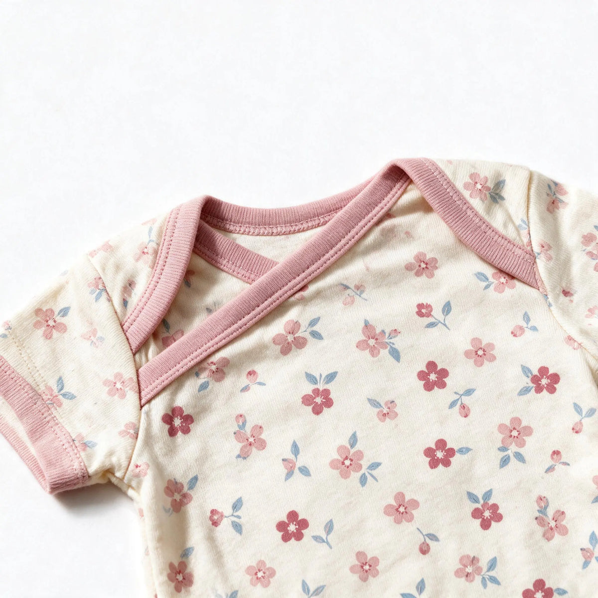 Close up photograph of the JOWI Soft Blossom Bodysuit on white: the envelope neckline, with the two shoulder panels crossing over each other under their plain dusty pink bands