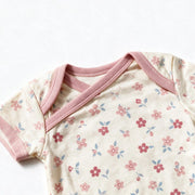 Close up photograph of the JOWI Soft Blossom Bodysuit on white: the envelope neckline, with the two shoulder panels crossing over each other under their plain dusty pink bands